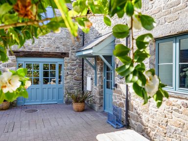 An outdoor stone patio with blue doors and windows framed by leafy branches at Trelawney Mawnan Smith Near Falmouth