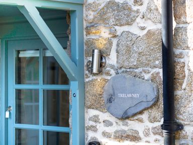 A close up of a stone wall with a metal light fixture and a sign reading Trelawney next to a blue wooden door frame at Trelawney Mawnan Smith Near Falmouth