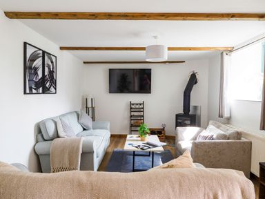 A living room with sofas a coffee table a wall-mounted TV and a wood-burning stove at Trelawney Mawnan Smith Near Falmouth