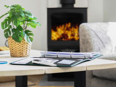 A table with a plant in a basket and an open binder with papers in a living room with a fireplace and a sofa at Trelawney in Mawnan Smith Near Falmouth