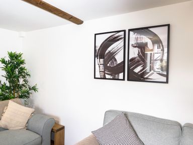 A living room with two grey sofas a wooden side table green plant and abstract black and white paintings on the wall at Trelawney Mawnan Smith Near Falmouth