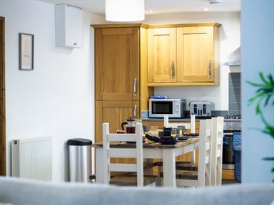 A kitchen with wooden cabinets a dining table with chairs and kitchen appliances at Trelawney Mawnan Smith Near Falmouth