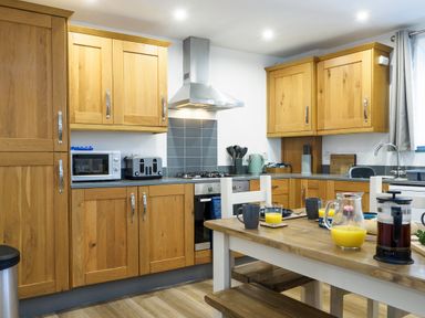 A kitchen with wooden cabinets dining table with drinks and cups at Trelawney in Mawnan Smith Near Falmouth