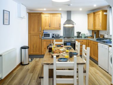 A kitchen with wooden cabinets and a dining table set with plates and glasses at Trelawney in Mawnan Smith Near Falmouth