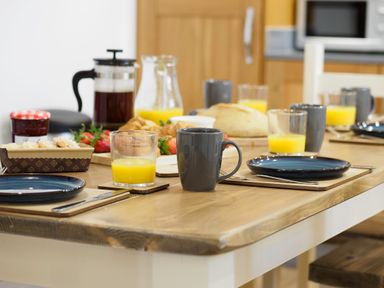 A wooden dining table set with plates mugs glasses of orange juice basket of bread croissants and a jar of jam at Trelawney Mawnan Smith Near Falmouth