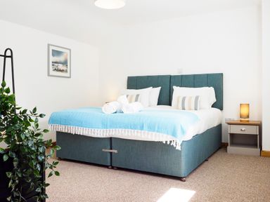 A bedroom with a double bed with a blue bedspread and white pillows a bedside table with a lamp and a plant on a stand at Trelawney in Mawnan Smith Near Falmouth