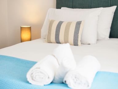 A bed with white pillows a striped pillow and rolled white towels on a blue blanket at Trelawney Mawnan Smith Near Falmouth