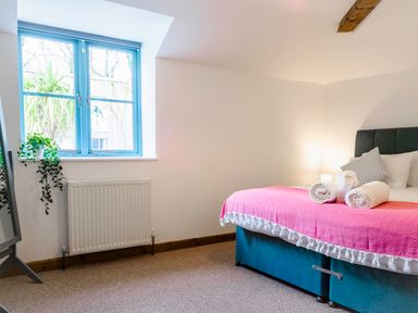 A bedroom with a bed covered with a pink blanket and white towels near a window with blue frames at Trelawney in Mawnan Smith Near Falmouth