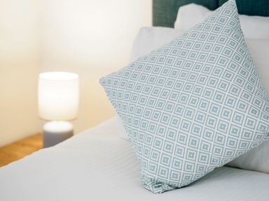 A close-up of a bed with a patterned pillow and a lit bedside lamp on a wooden table at Trelawney in Mawnan Smith Near Falmouth