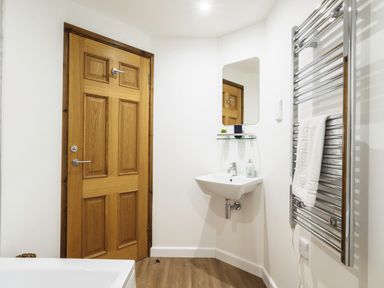 A bathroom with a wooden door a wall-mounted sink a mirror a towel rail with a towel and wooden floor at Trelawney in Mawnan Smith Near Falmouth