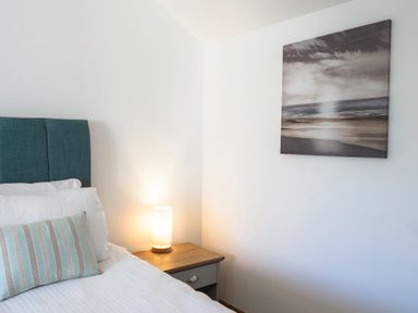 A bedroom corner with a bed, bedside table, lamp, and wall art at Trelawney in Mawnan Smith Near Falmouth