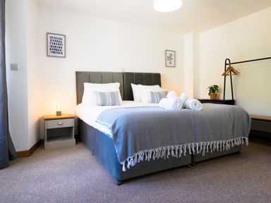 A bedroom with a double bed bedside tables a lamp wall art and a clothes rack at Trelawney Mawnan Smith Near Falmouth