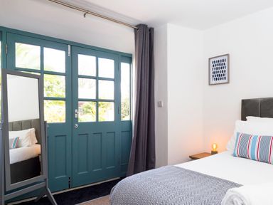 A bedroom with a bed bedside table lamp mirror and blue framed windows at Trelawney in Mawnan Smith Near Falmouth
