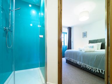 A shower area with turquoise walls next to a bedroom with a bed and a window at Trelawney in Mawnan Smith Near Falmouth