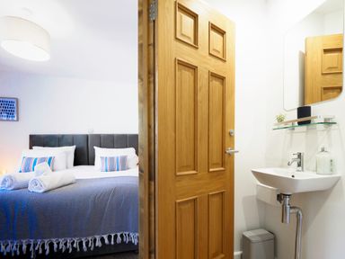 A bedroom with a bed and rolled towels next to a bathroom with a sink and mirror at Trelawney in Mawnan Smith Near Falmouth