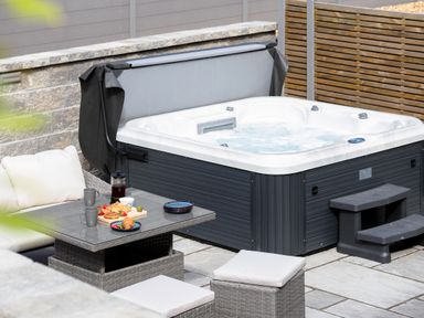 An outdoor seating area with a hot tub a table with breakfast items and cushioned chairs at Trelawney in Mawnan Smith Near Falmouth