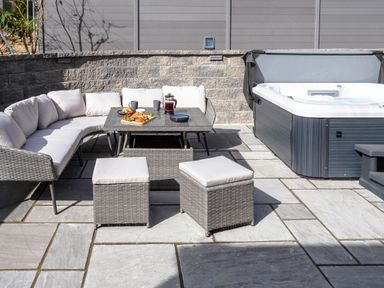 An outdoor patio with a sectional sofa table two cushioned stools and a hot tub