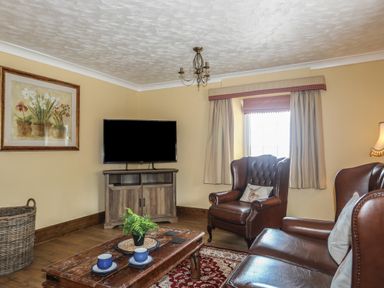 A living room with leather armchairs a wooden coffee table with cups a television and a window at Frongoch Cottage in Red Wharf Bay near Pentraeth