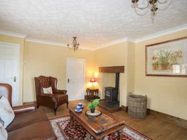 A living room with leather chairs wooden coffee table stove and floral painting at Frongoch Cottage in Red Wharf Bay near Pentraeth