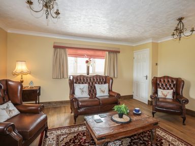 A living room with leather armchairs a wooden coffee table and a window with curtains at Frongoch Cottage Red Wharf Bay near Pentraeth