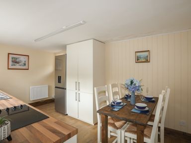 A kitchen and dining area with a wooden table set with dishes and a vase of flowers at Frongoch Cottage in Red Wharf Bay near Pentraeth