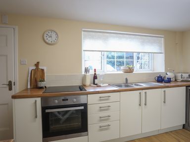 A kitchen with oven stove countertop sink and window with a roller blind at Frongoch Cottage in Red Wharf Bay near Pentraeth