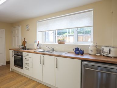 A kitchen with white cabinets a wooden countertop a sink a blue teapot set a white kettle and a toaster at Frongoch Cottage in Red Wharf Bay near Pentraeth