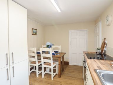 A kitchen with a wooden dining table and white chairs a stove a sink and cabinets at Frongoch Cottage Red Wharf Bay near Pentraeth