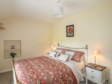 A bedroom with a bed with red patterned bedding two bedside tables with lamps and a small painting on the wall at Frongoch Cottage Red Wharf Bay near Pentraeth