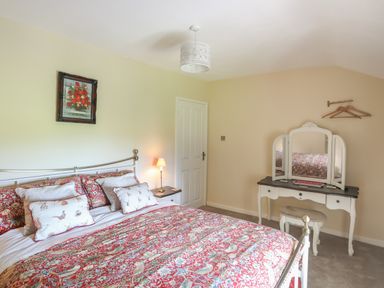 A bedroom with a bed with patterned bedding a bedside table with a lamp a dressing table with a vanity mirror and a stool at Frongoch Cottage in Red Wharf Bay near Pentraeth