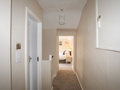 A hallway with a light fixture ceiling light switch doors and a view into a bedroom at Frongoch Cottage in Red Wharf Bay near Pentraeth