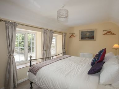 A bedroom with a bed by two windows with curtains and a painting on the wall at Frongoch Cottage in Red Wharf Bay near Pentraeth