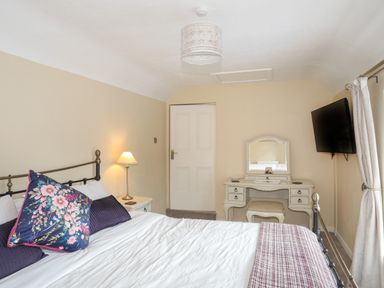 A bedroom with a bed pillows bedside table lamp dressing table stool and wall mounted television at Frongoch Cottage in Red Wharf Bay near Pentraeth