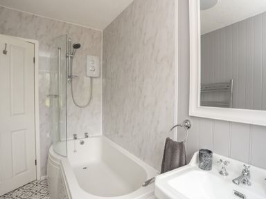 A bathroom with a bathtub shower unit and a sink with mirror at Frongoch Cottage in Red Wharf Bay near Pentraeth