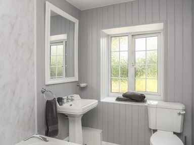 A bathroom with a sink, toilet, window, mirror, and towels at Frongoch Cottage Red Wharf Bay near Pentraeth