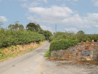 A country road lined with hedges and a stone wall with a sign for Fron Goch private road at Frongoch Cottage in Red Wharf Bay near Pentraeth