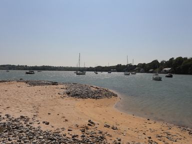 A shoreline with sand and rocks with boats on the water and houses along the shore at Frongoch Cottage in Red Wharf Bay near Pentraeth