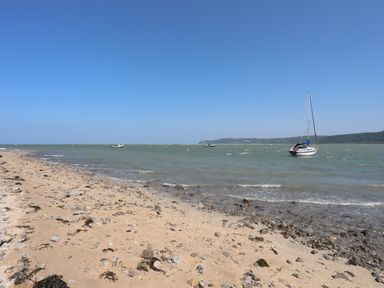 A sandy and rocky beach with boats on the water and hills in the distance at Frongoch Cottage in Red Wharf Bay near Pentraeth