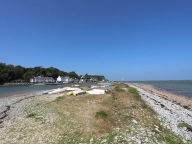 A shoreline with boats on land and houses near trees at Frongoch Cottage in Red Wharf Bay near Pentraeth