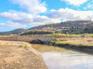 A stone bridge over a river with hills and trees in the background at Frongoch Cottage in Red Wharf Bay near Pentraeth