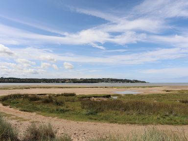 A coastal landscape with sand, grass, and water under a partly cloudy sky at Frongoch Cottage in Red Wharf Bay near Pentraeth