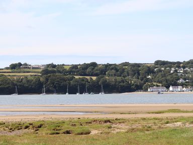 A river with sailboats and boats on the water and houses and trees on the opposite shore at Frongoch Cottage in Red Wharf Bay near Pentraeth