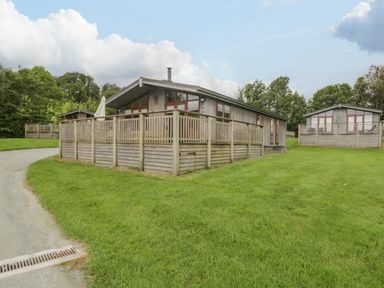 Two wooden lodges with fenced decks on a grassy area with trees in the background at Rivendell Lodge in Roger Ground near Hawkshead