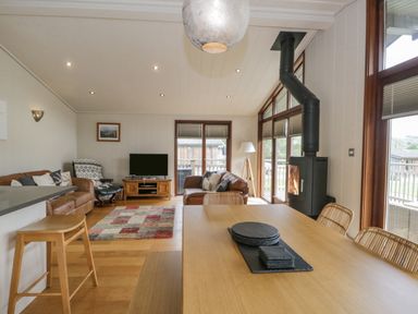 A living room with a wooden dining table and chairs a stove a television and leather sofas at Rivendell Lodge in Roger Ground near Hawkshead