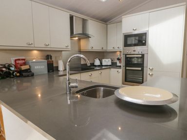 A kitchen with a sink and faucet on a countertop a plate on the countertop cabinets and built-in appliances in the background at Rivendell Lodge Roger Ground near Hawkshead
