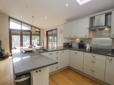 A kitchen with white cabinets a gray countertop a sink stove and a dining table with chairs at Rivendell Lodge in Roger Ground near Hawkshead