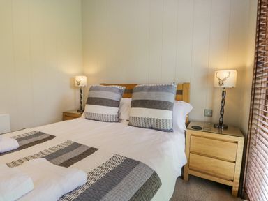 A bedroom with a wooden bed and bedside tables with lamps at Rivendell Lodge in Roger Ground near Hawkshead
