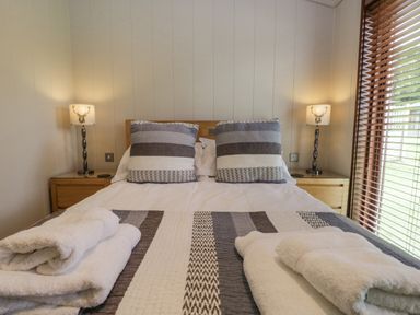 A bedroom with a bed two bedside tables two lamps and towels on the bed at Rivendell Lodge Roger Ground near Hawkshead