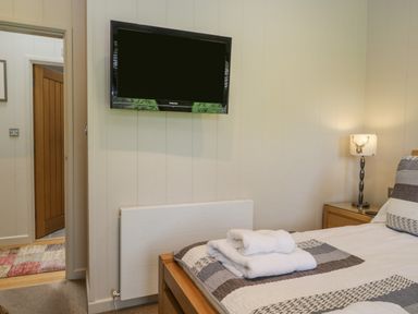 A bedroom with a wall-mounted TV folded towels on a bed and a bedside lamp at Rivendell Lodge in Roger Ground near Hawkshead