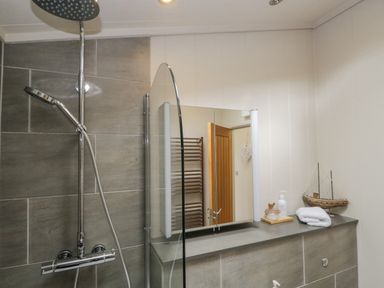 A bathroom with a shower, mirror, folded towels, soap dispenser, and a decorative boat model at Rivendell Lodge in Roger Ground near Hawkshead